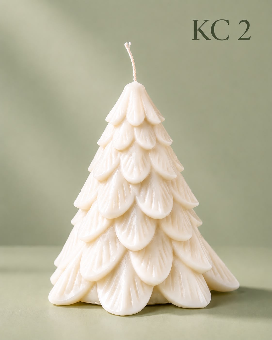 Cream Christmas tree mould candle with tiered, petal-shaped branches and a twisted wick, standing against a sage green backdrop